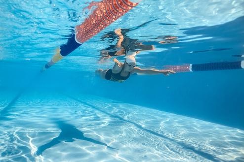 Schwimmerin taucht unter Wasser, während sie die Hand ausstreckt und sich durch das blaue Wasser bewegt.